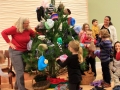 Children, youth and parents decorating the Mitten Tree with hats, scarves, gloves and mittens.